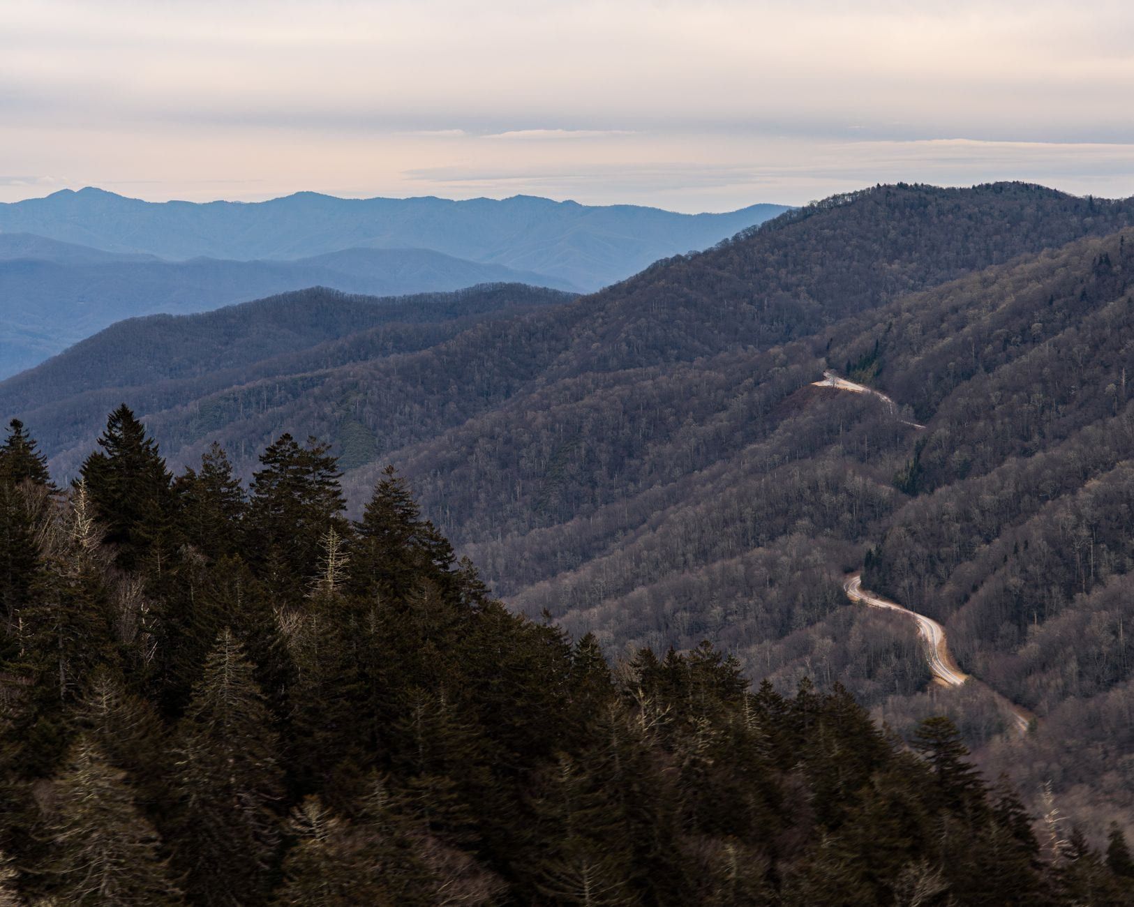 A winding paved road cuts across forested ridges in the Great Smoky Mountains under a pale sky.